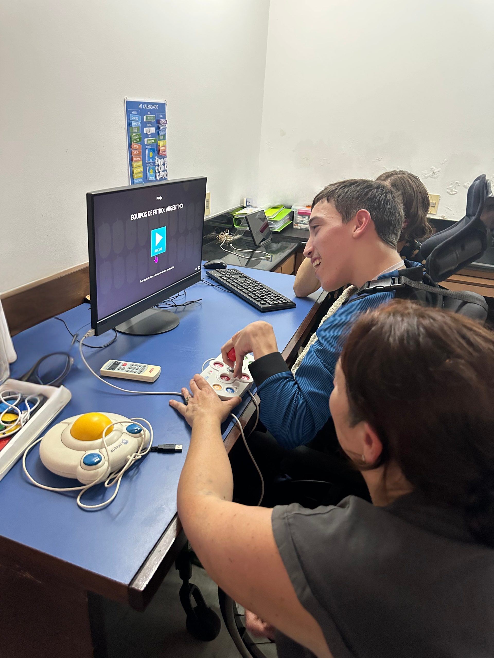 Joven utilizando tecnología asistiva frente a una computadora, acompañada por dos personas durante una actividad.