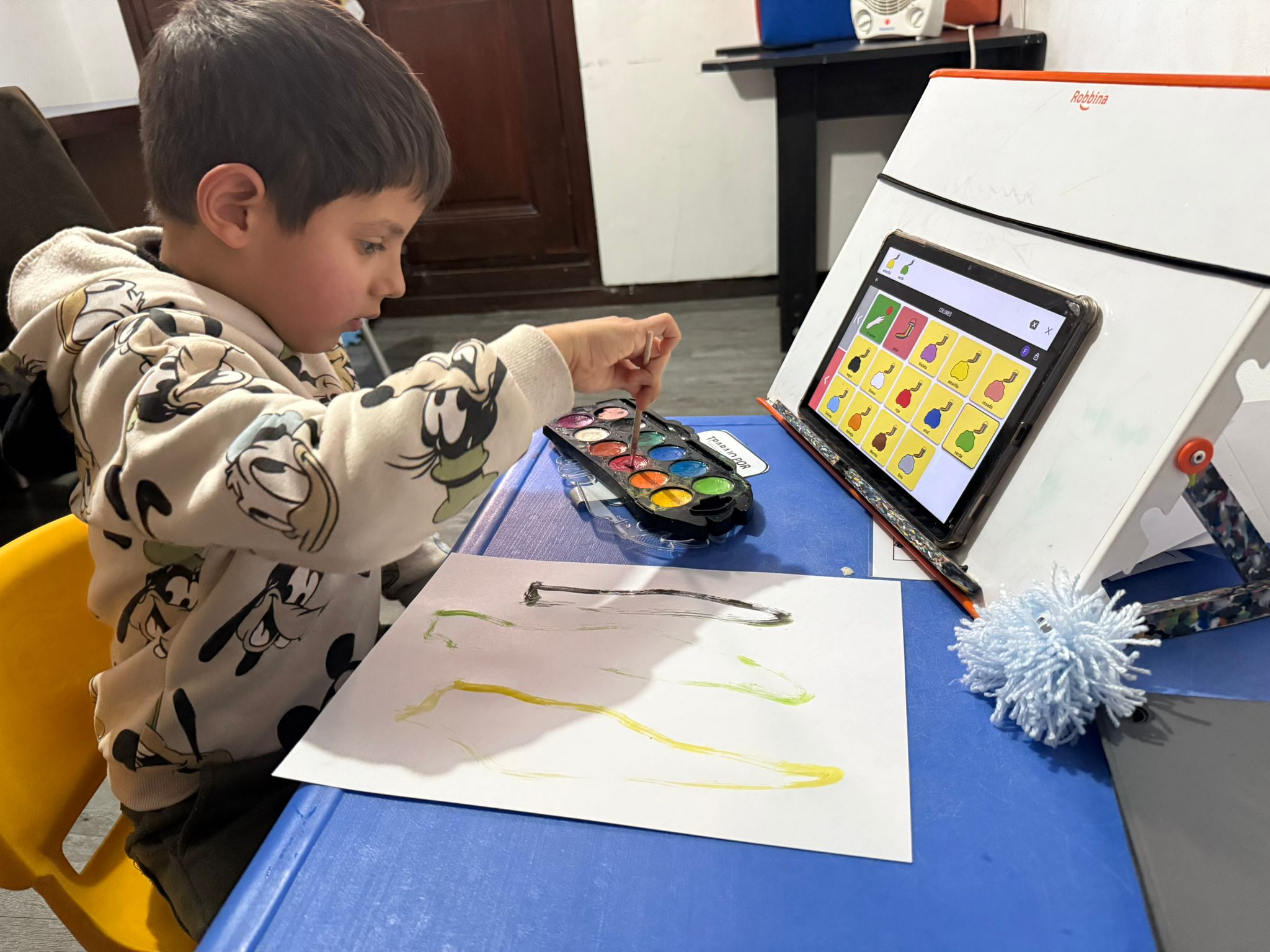 Niño realiza una actividad de pintura mientras utiliza una tablet con un sistema de comunicación visual